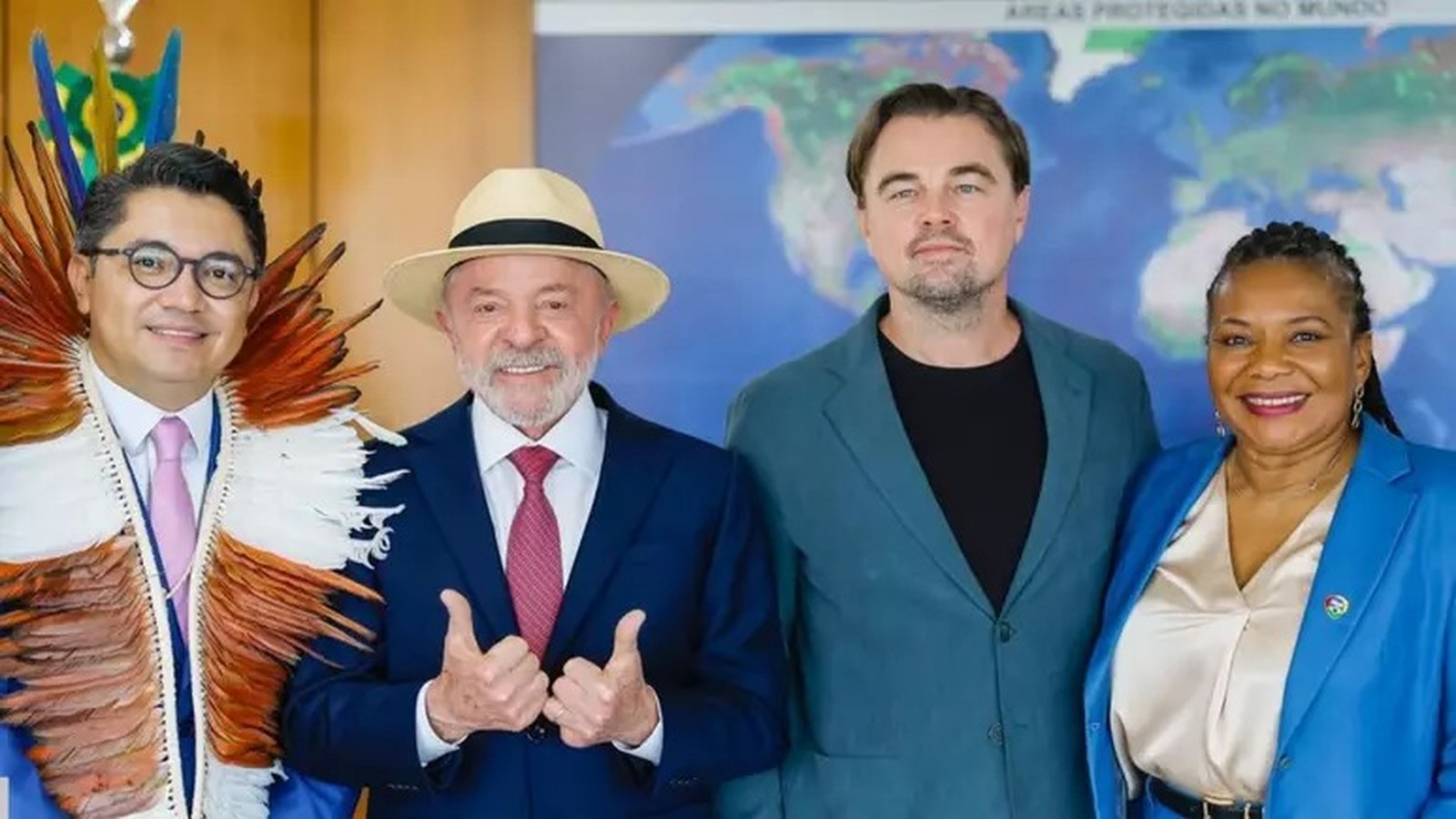 Lula de chapéu com polegares para cima, DiCaprio, Eloy Terena com adereço indígena e Margareth Menezes sorriem