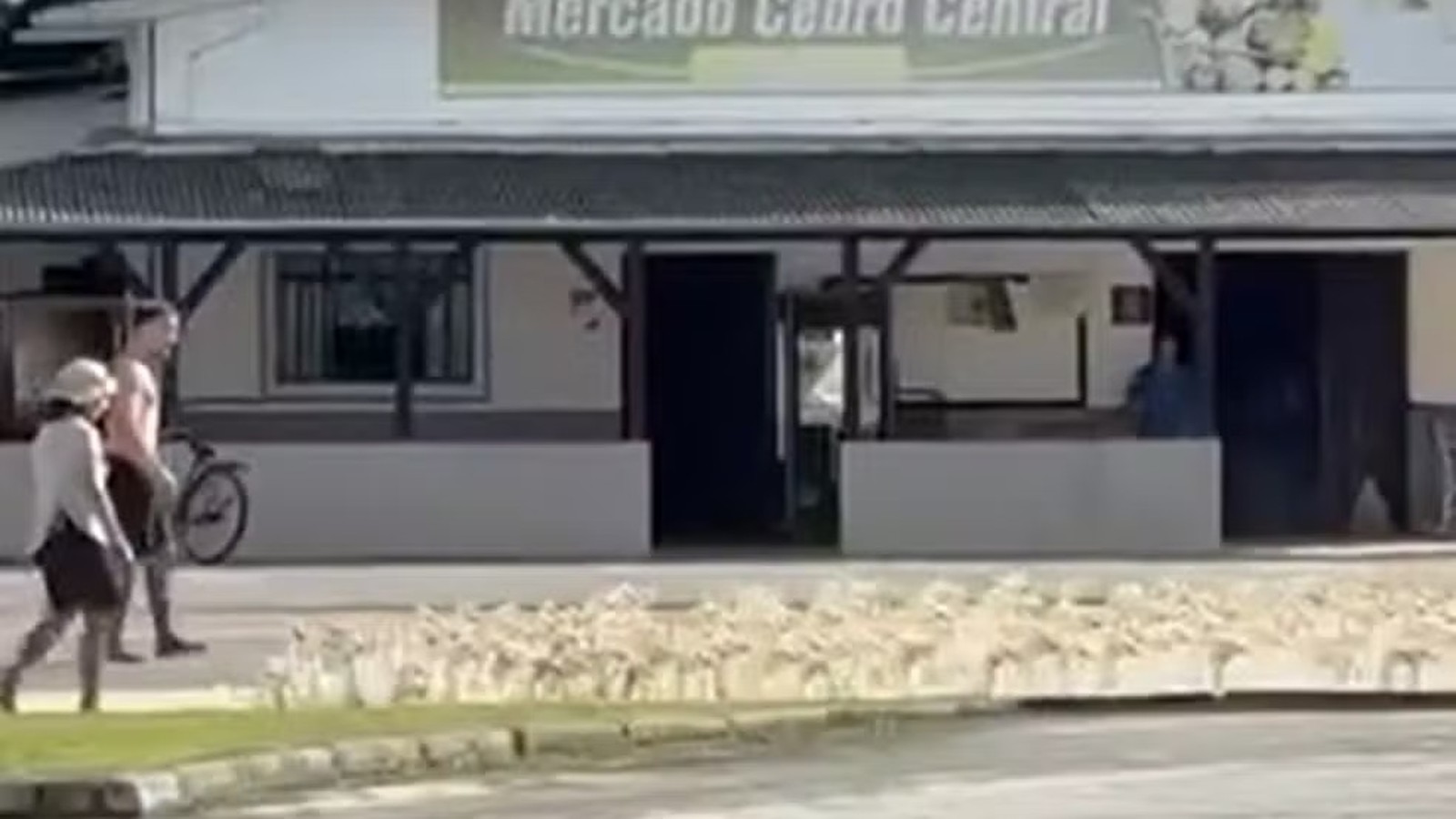 Duas pessoas com bicicleta na rua em frente ao Mercado Cedro Central.