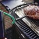 Termômetro digital marca 44.9°C, com sonda espetada em carne assando na churrasqueira.