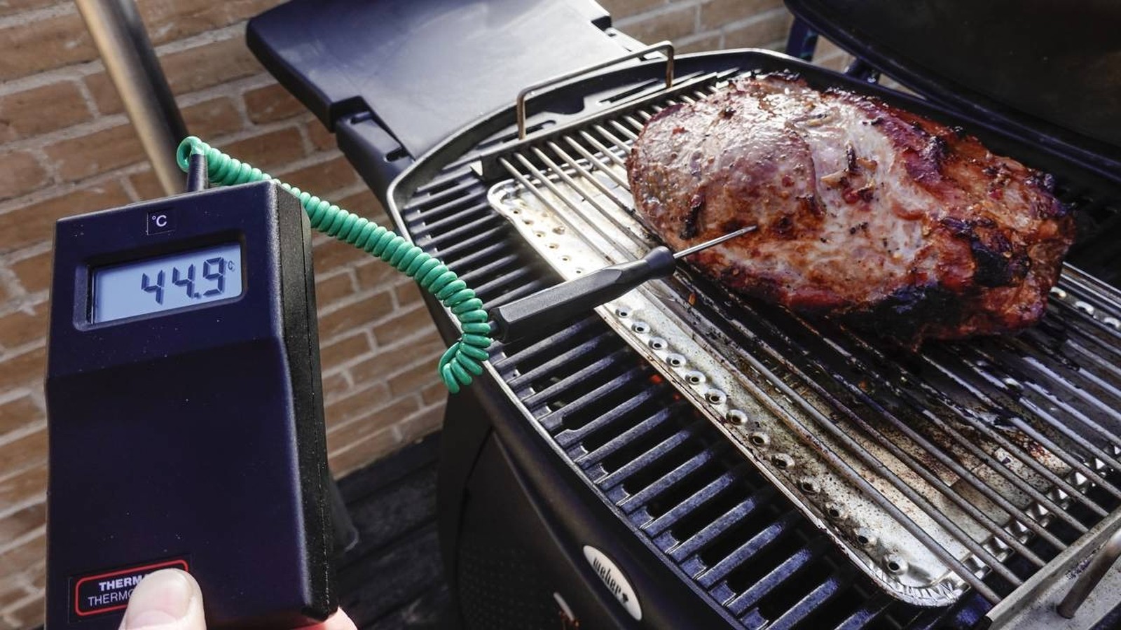 Termômetro digital marca 44.9°C, com sonda espetada em carne assando na churrasqueira.