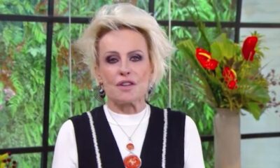 Ana Maria Braga com cabelo loiro, maquiagem escura e colar, em estúdio com plantas