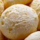 Close-up de vários pães de queijo redondos, recém-assados, com superfície rachada e clara
