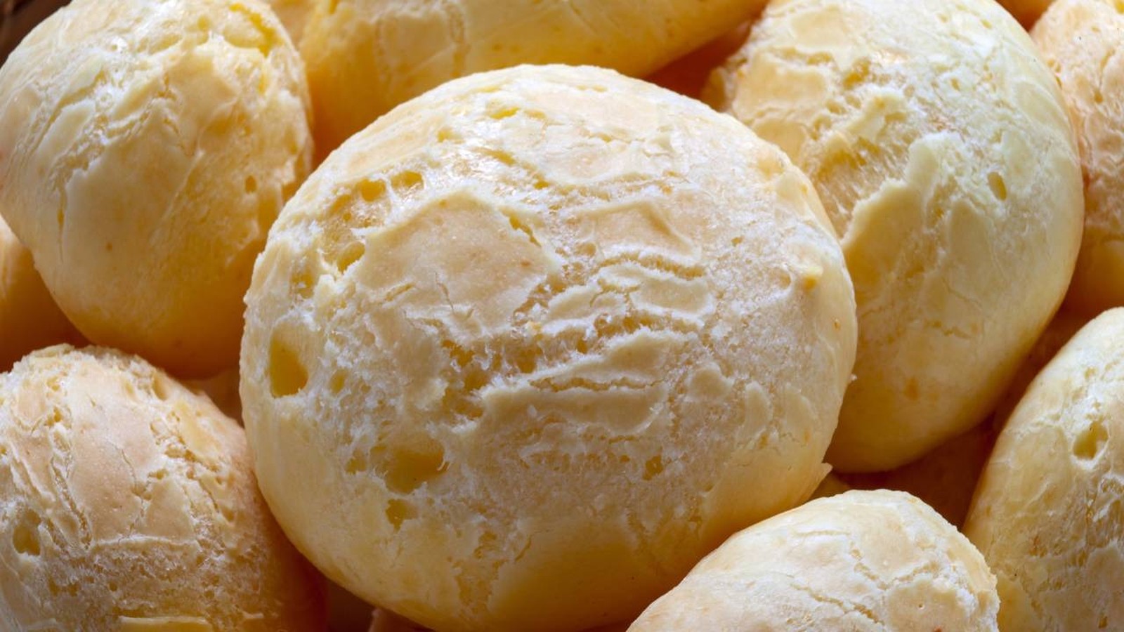 Close-up de vários pães de queijo redondos, recém-assados, com superfície rachada e clara