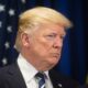 Close-up de Donald Trump com terno escuro e gravata em frente a bandeira dos EUA