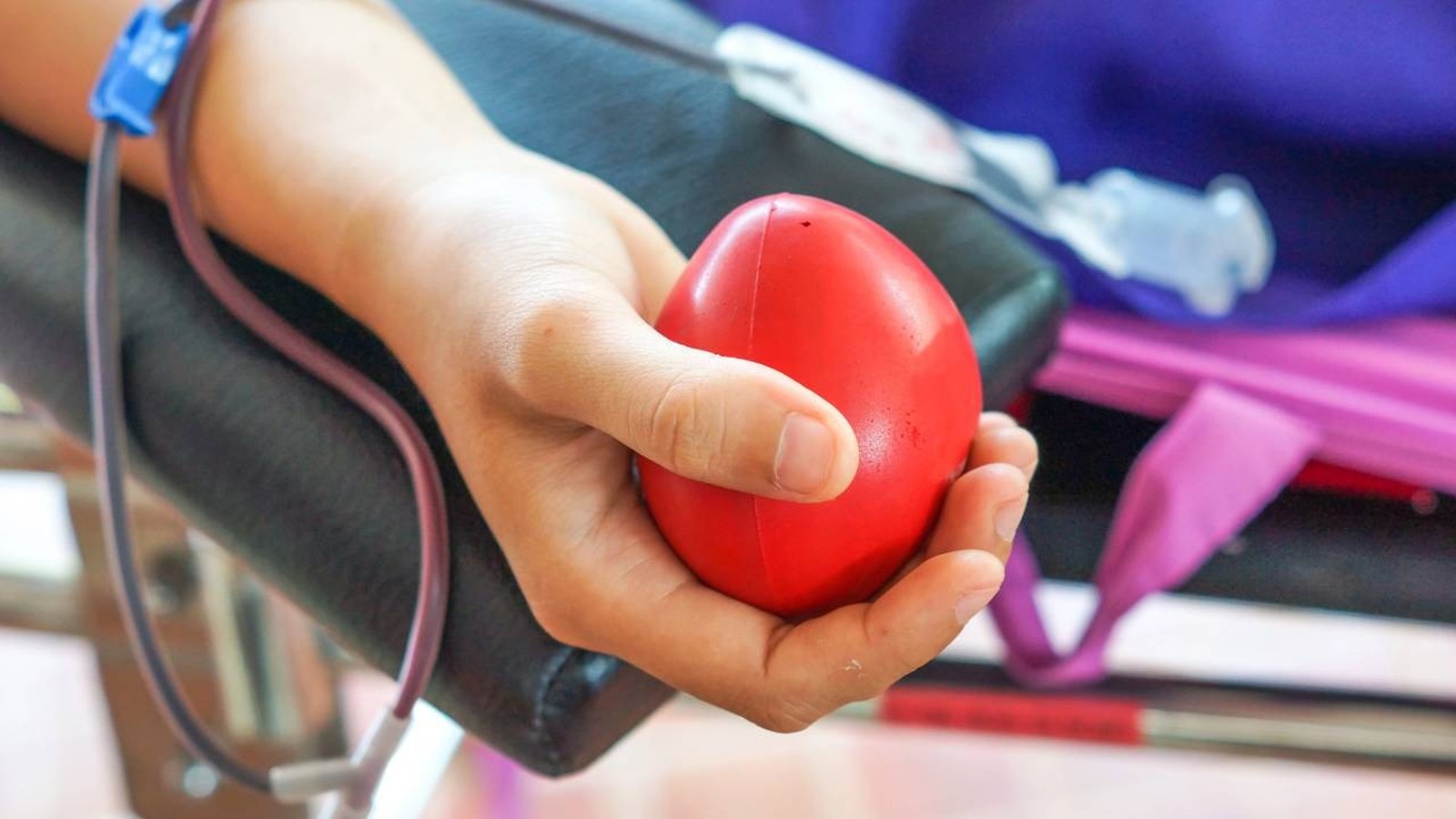 Close-up de um braço doando sangue, segurando uma bola vermelha de apertar