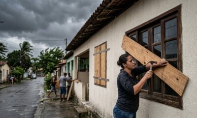 Mulher de camiseta escura martela tábua de madeira em janela sob céu cinza e rua molhada
