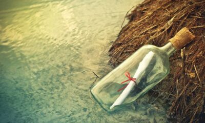 Garrafa de vidro com mensagem de papel enrolado e fita vermelha na água e areia