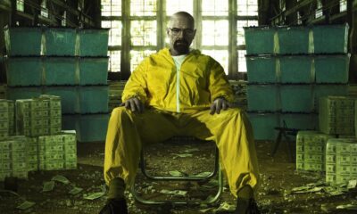 Walter White de Breaking Bad em traje amarelo, sentado, rodeado por dinheiro e metanfetamina azul.