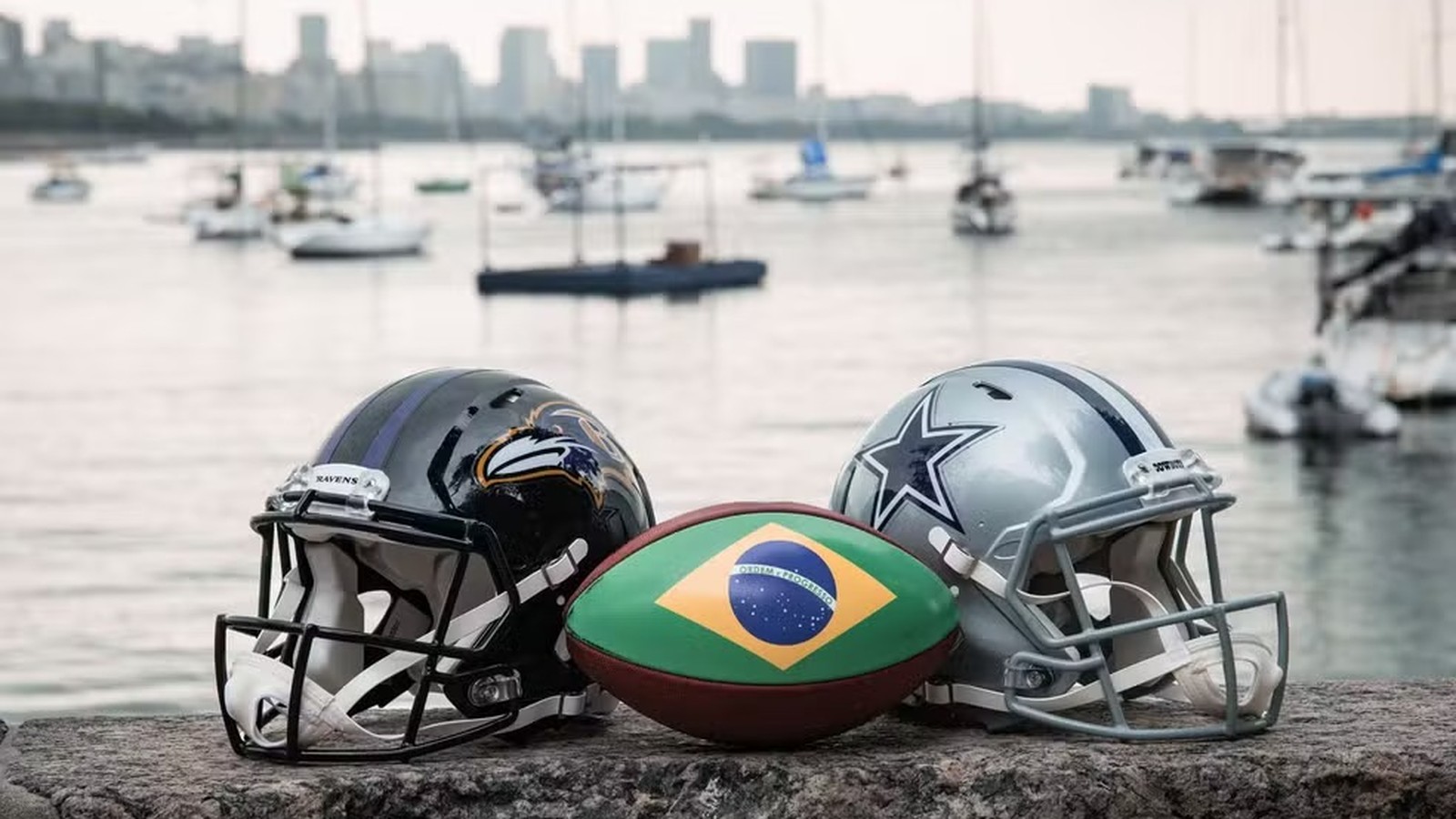 Capacete dos Ravens, capacete dos Cowboys e bola com bandeira do Brasil na orla