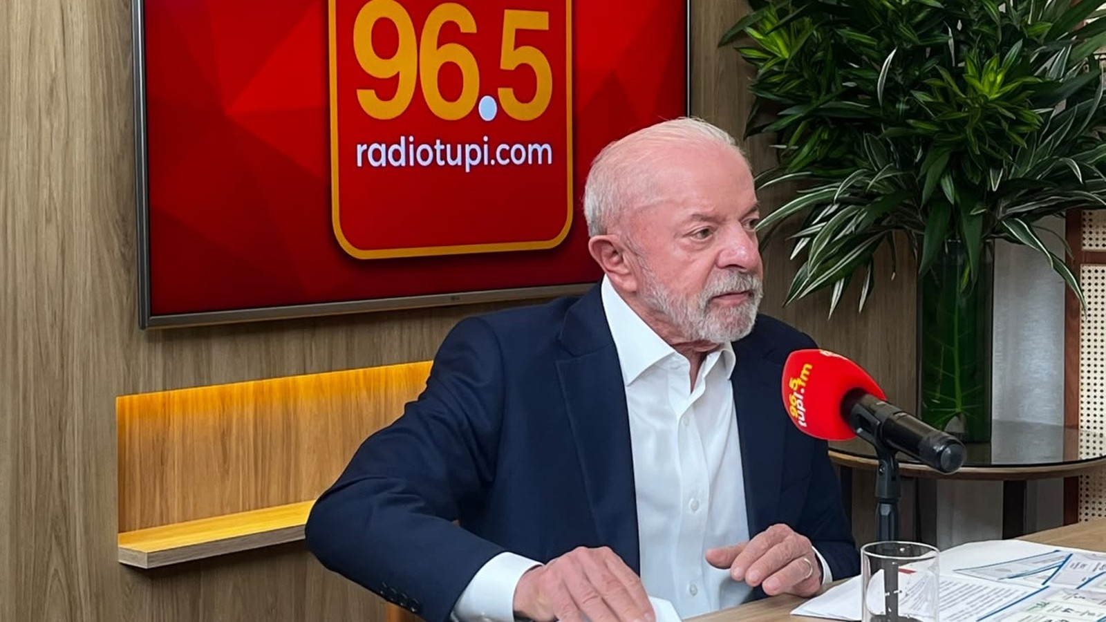 Luiz Inácio Lula da Silva fala em microfone vermelho da Rádio Tupi. Fundo com logo 96.5