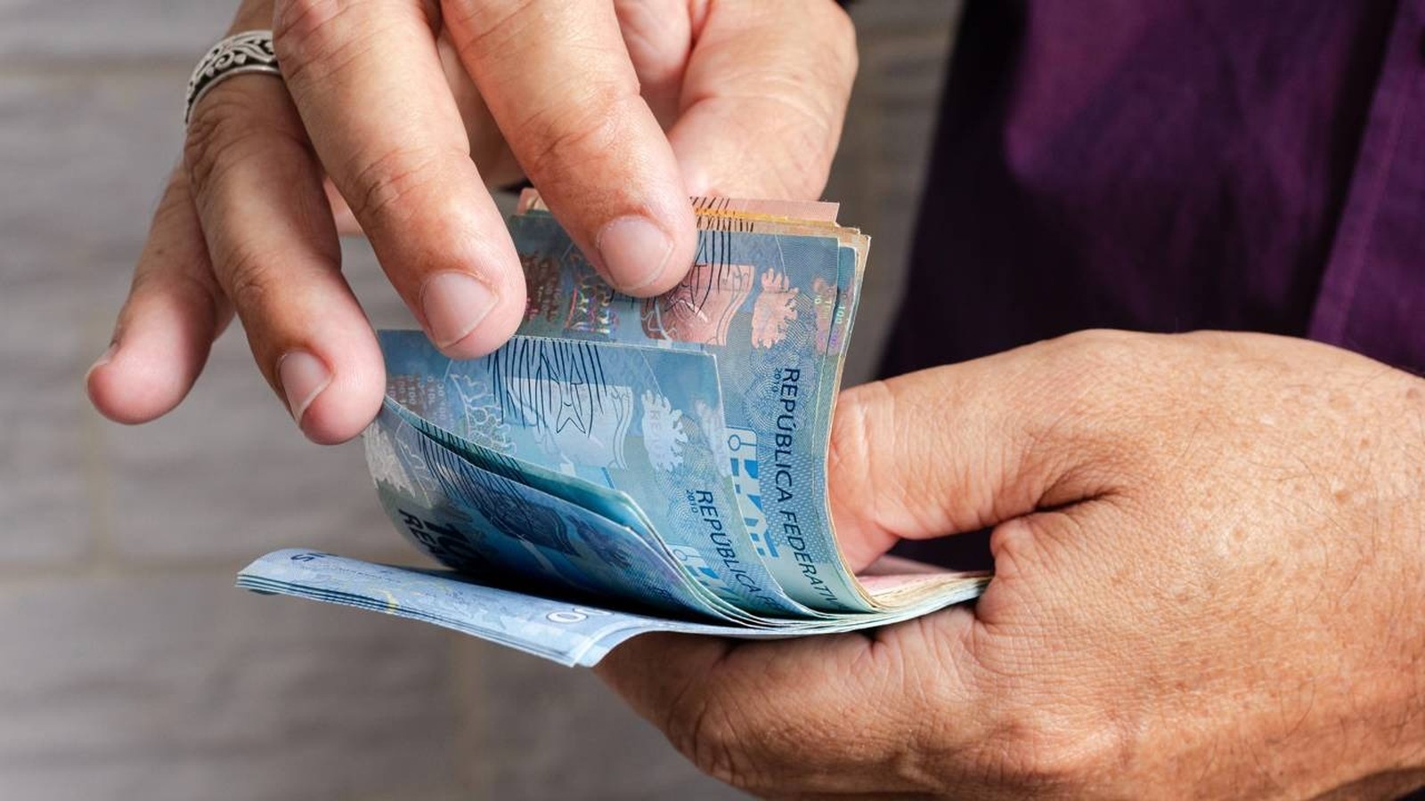Mãos seguram e contam cédulas de dinheiro brasileiro