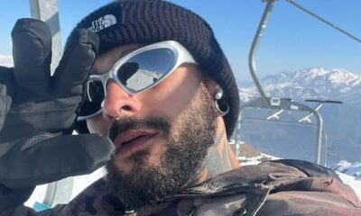 Homem com óculos espelhados, gorro preto, barba e luvas em montanha nevada com teleférico