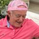 Renato Aragão de camisa polo rosa e boné rosa, sorrindo e olhando para baixo
