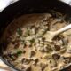 Close-up de strogonoff cremoso com frango e champignon em panela de ferro com colher de madeira