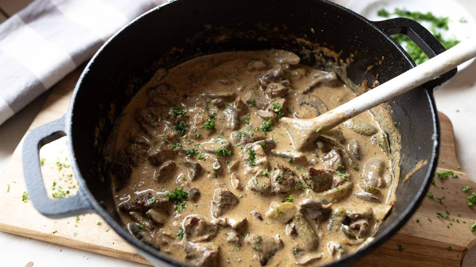 Close-up de strogonoff cremoso com frango e champignon em panela de ferro com colher de madeira