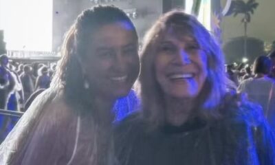 Duas mulheres sorrindo em primeiro plano, uma com capa de chuva clara, outra escura