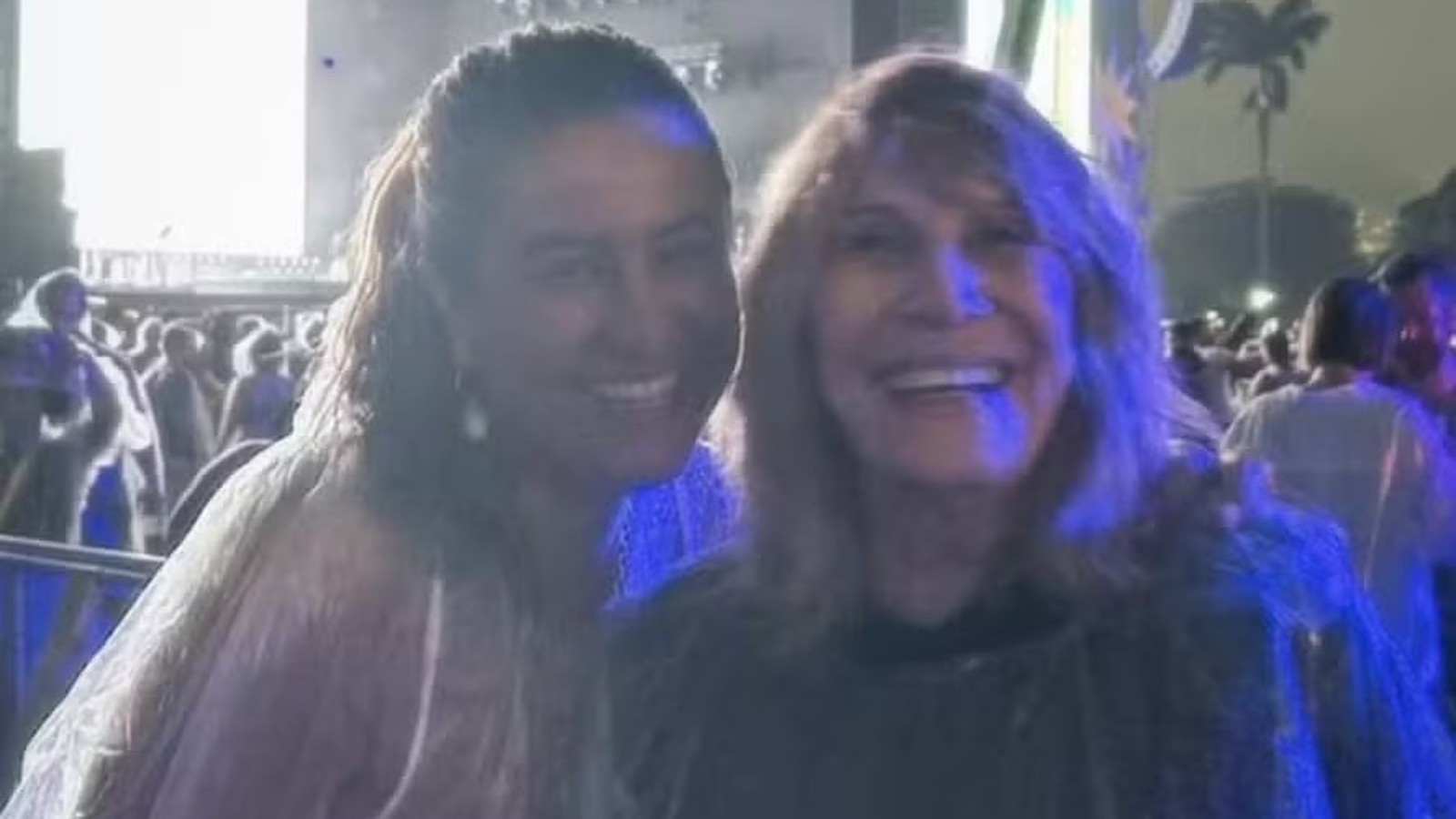 Duas mulheres sorrindo em primeiro plano, uma com capa de chuva clara, outra escura
