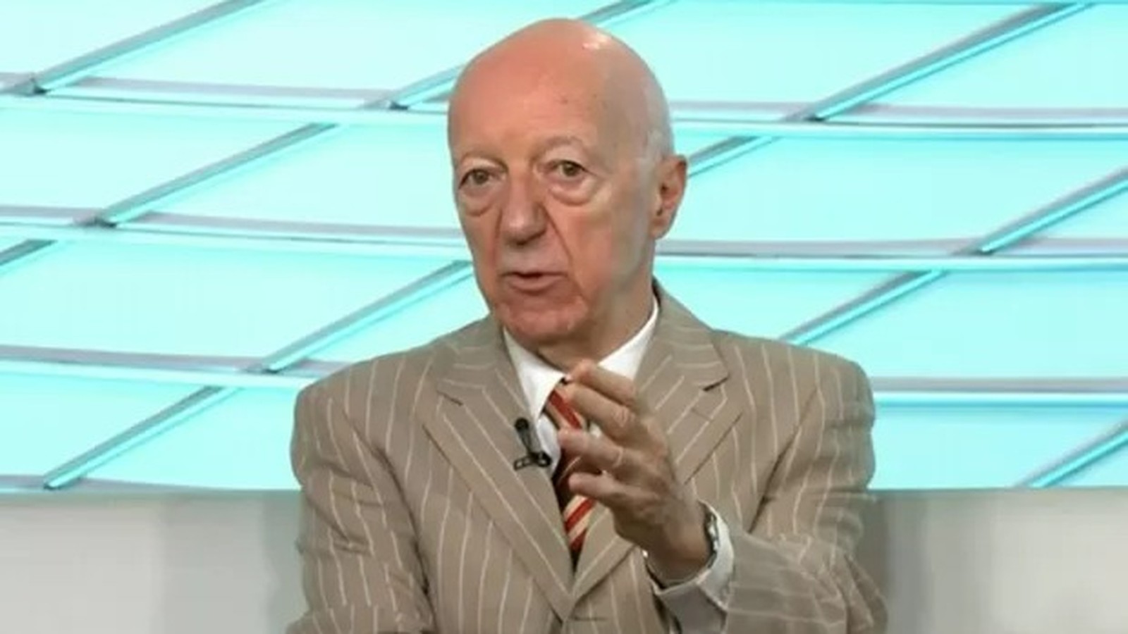 Claudio Carsughi, homem careca de terno listrado, gesticula em estúdio de TV