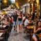 Dono de bar coloca mesas e cadeiras na calçada para atender mais clientes, deixa passagem estreita para pedestres e acaba recebendo multa de R$ 2 mil após fiscalização no local