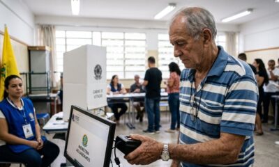 Homem idoso escaneia digital em leitor biométrico no TRE, tela mostra "Biometria Aguardando"