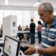 Homem idoso escaneia digital em leitor biométrico no TRE, tela mostra "Biometria Aguardando"