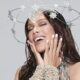 Anitta sorri com olhos fechados, mãos no rosto, usando coroa de estrelas e joias