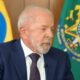 Luiz Inácio Lula da Silva, cabelo e barba brancos, terno azul e gravata, entre bandeiras do Brasil