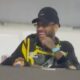 Neymar de boné, óculos e camisa preta e amarela rindo em um camarote