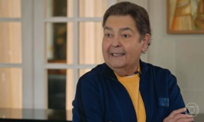 Fausto Silva em entrevista, jaqueta azul e camiseta amarela, com logo da Globo