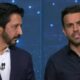 Dois homens em estúdio de TV, um de terno e outro de camisa escura, ambos com microfones
