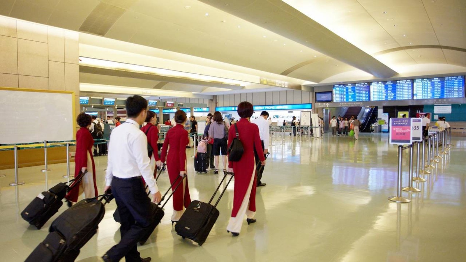 Pessoas, incluindo tripulação de voo em uniformes vermelhos, caminham com malas em aeroporto