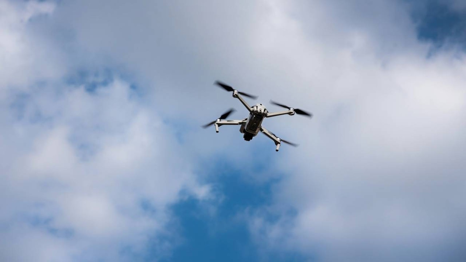 Drone branco voando em céu azul claro com nuvens espalhadas