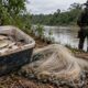Peixes em cooler, rede de pesca no chão, policial militar e barco à beira de rio