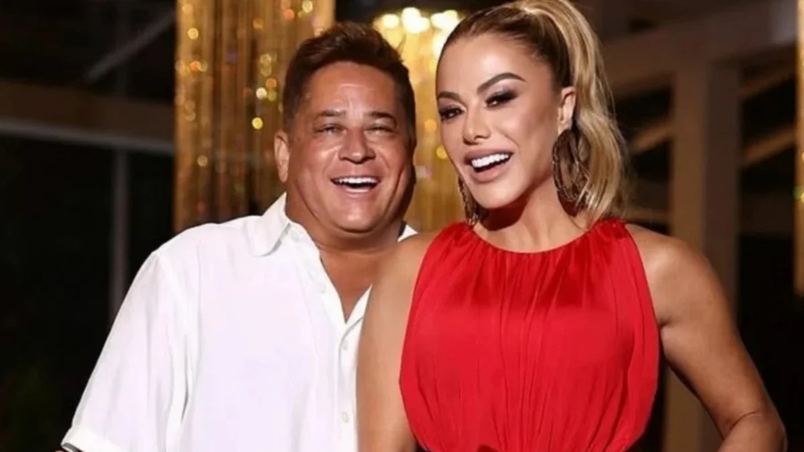 Leonardo e Poliana Rocha sorriem amplamente, ele de camisa branca, ela de vestido vermelho