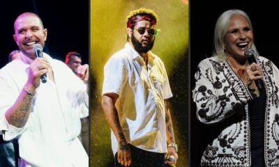Três cantores no palco: homem sorrindo, homem com barba e óculos, e mulher com cabelo branco