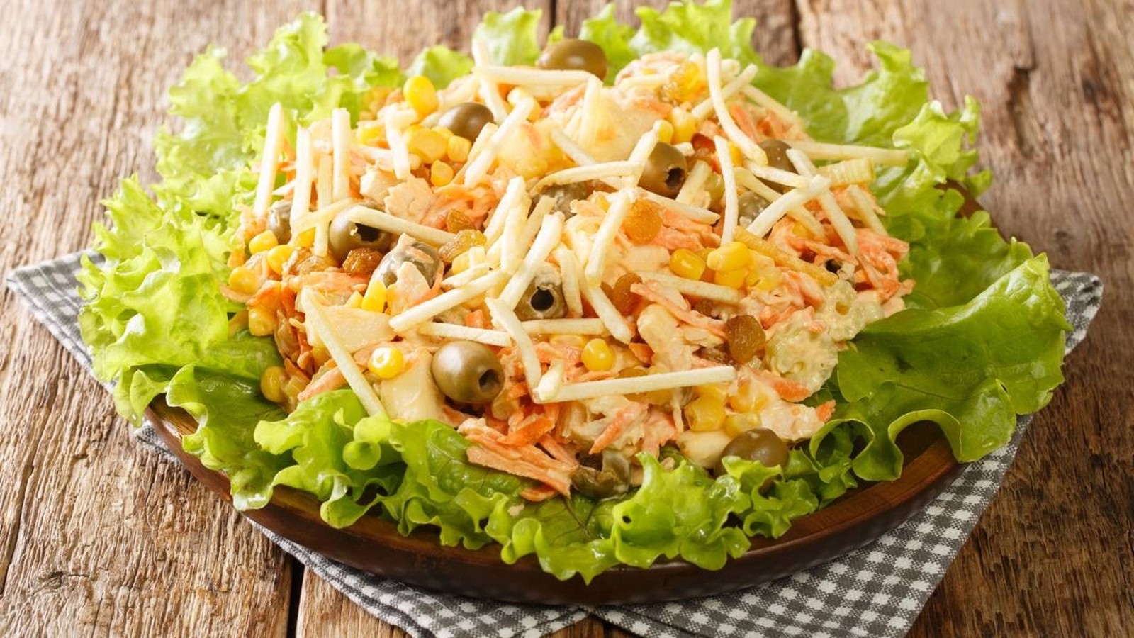Salpicão de frango com batata palha, milho, azeitonas, uva passa, cenoura e alface em uma travessa