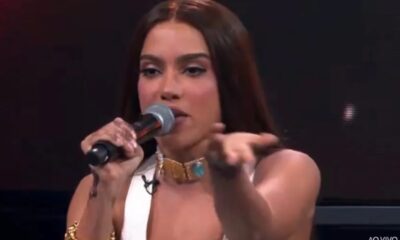Anitta segura microfone, gesticulando, em programa "AO VIVO" na TV