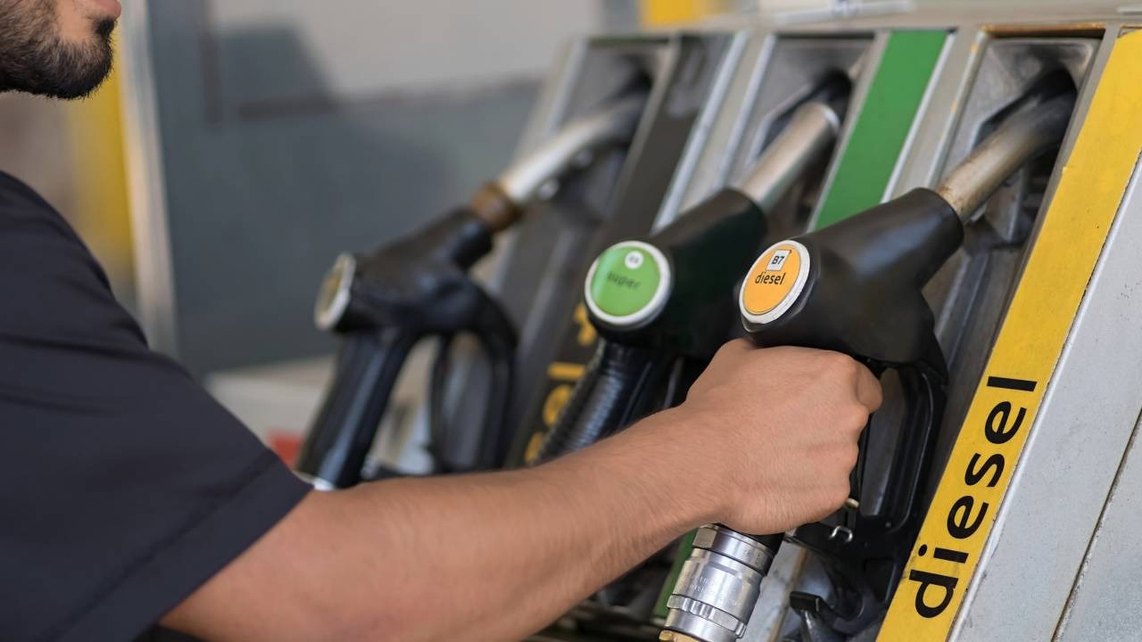 Mão segura bico de bomba de combustível 'B7 diesel' em posto, com 'diesel' visível