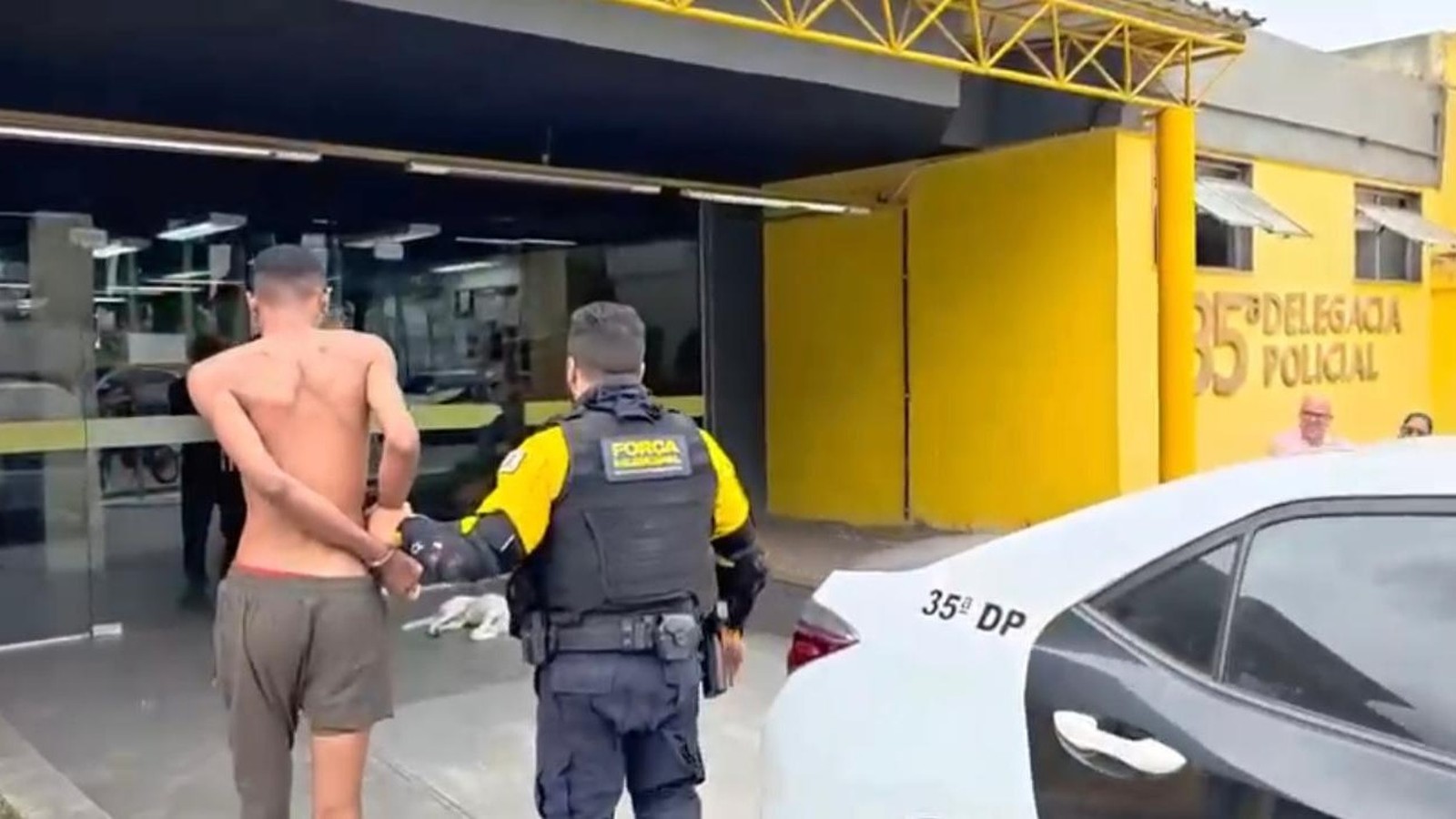 Policial da Força Municipal conduz homem algemado para delegacia com placa '35ª Delegacia Policial'
