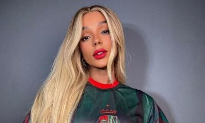 Brunna Gonçalves com cabelo longo loiro, batom vermelho e camisa verde e vermelha