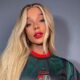 Brunna Gonçalves com cabelo longo loiro, batom vermelho e camisa verde e vermelha