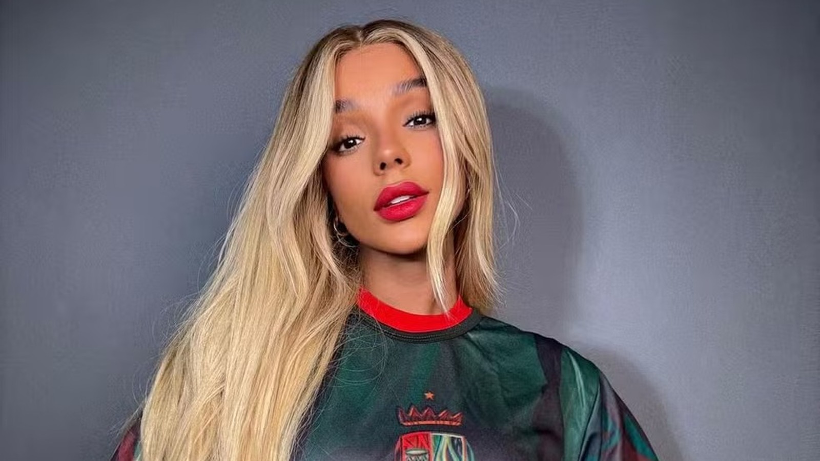 Brunna Gonçalves com cabelo longo loiro, batom vermelho e camisa verde e vermelha