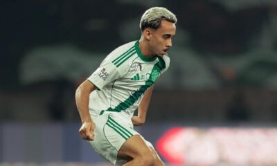 Jogador Matheus Gonçalves em campo com uniforme branco e verde, cabelo claro