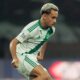 Jogador Matheus Gonçalves em campo com uniforme branco e verde, cabelo claro
