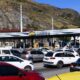 Praça de pedágio LAMSA com múltiplos carros em fila sob estrutura e montanhas