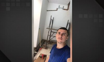 Jovem com camiseta azul tira selfie em cômodo em reforma com andaimes e ferramentas