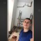 Jovem com camiseta azul tira selfie em cômodo em reforma com andaimes e ferramentas