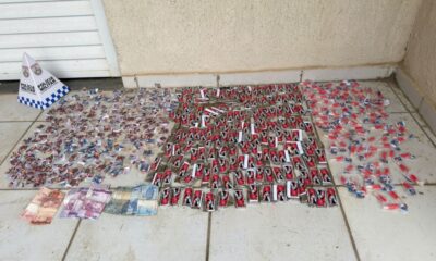 Drogas em embalagens diversas, notas de dinheiro e cone da Polícia Militar em piso claro
