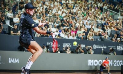João Fonseca em quadra de saibro com uniforme preto rebatendo bola no Rio Open