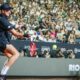João Fonseca em quadra de saibro com uniforme preto rebatendo bola no Rio Open